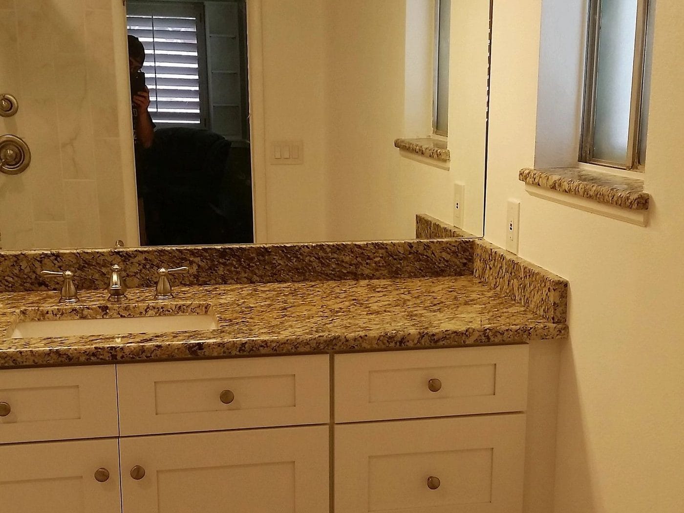 A bathroom vanity with a granite top and a full-width mirror