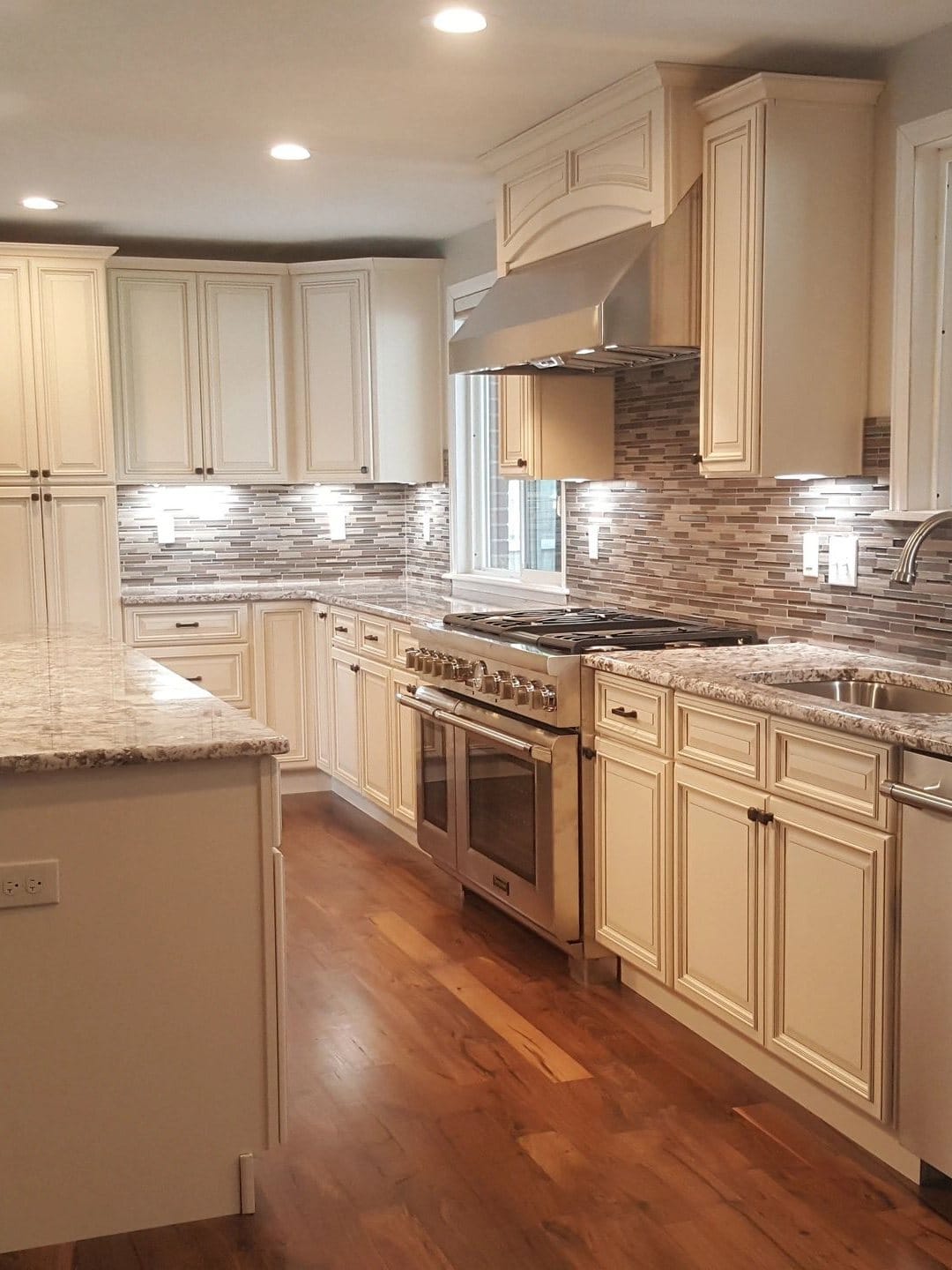 A finished kitchen remodel with cream cabinetry, a granite island and a hardwood floor